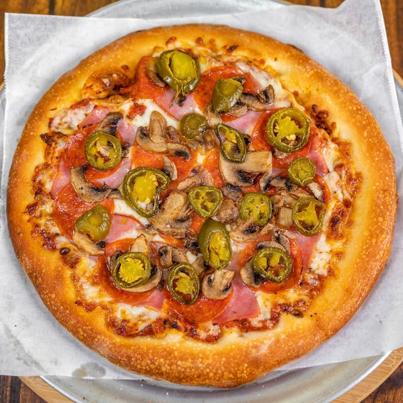 La Pizzeria's pizza with pepperoni, ham, mushrooms, and jalapeños on parchment paper.