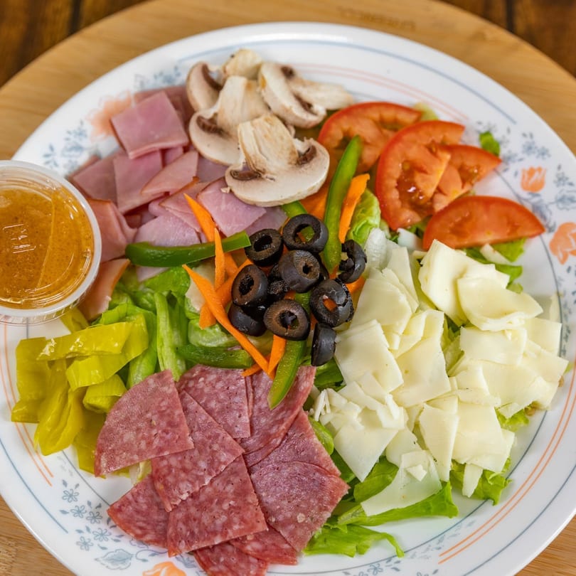A large La Pizzeria antipasto salad with ham, salami, cheese, tomatoes, olives, mushrooms, and dressing.